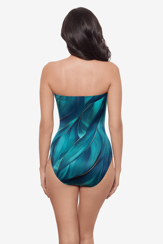 Woman turned away wearing a multi-blue bandeau one-piece swimsuit with gold detail