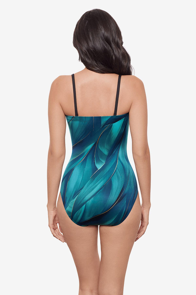 Woman turned away wearing a multi-blue bandeau one-piece swimsuit with gold detail