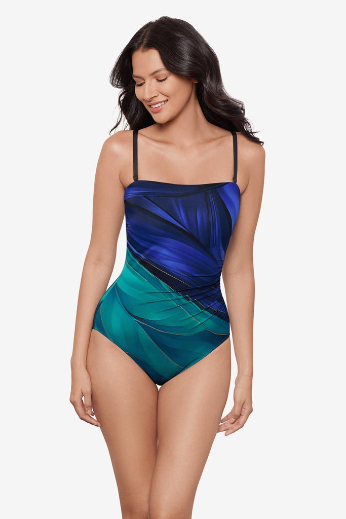 Woman wearing a multi-blue bandeau one-piece swimsuit with gold detail