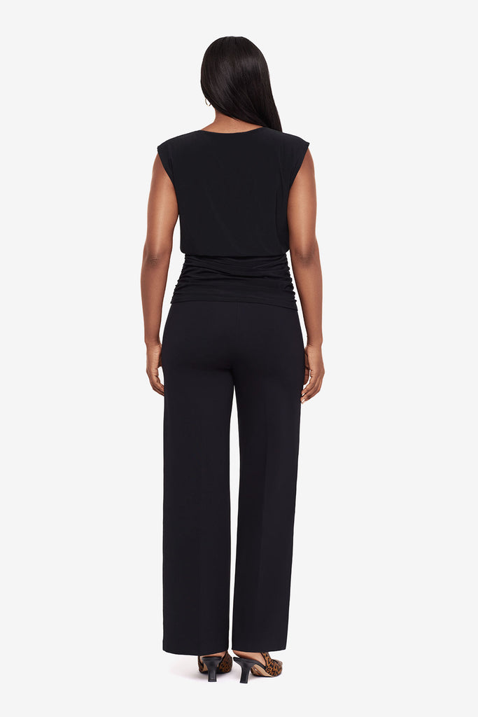 Woman in a black high neck blouse with matching wide leg pants turned away 