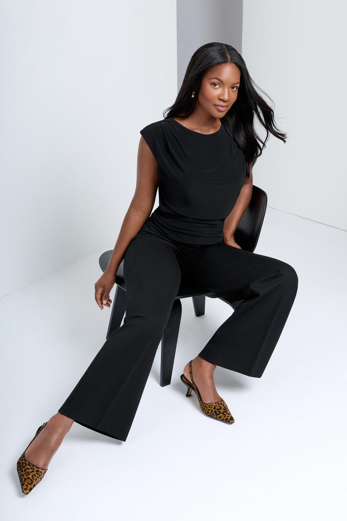 Woman sitting in chair wearing a black highneck blouse with matching wide leg pants