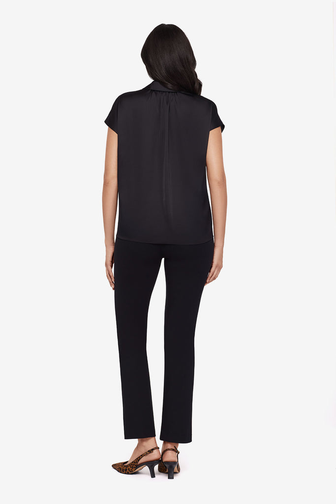 Woman turned away wearing a black blouse with matching black slim fit pants