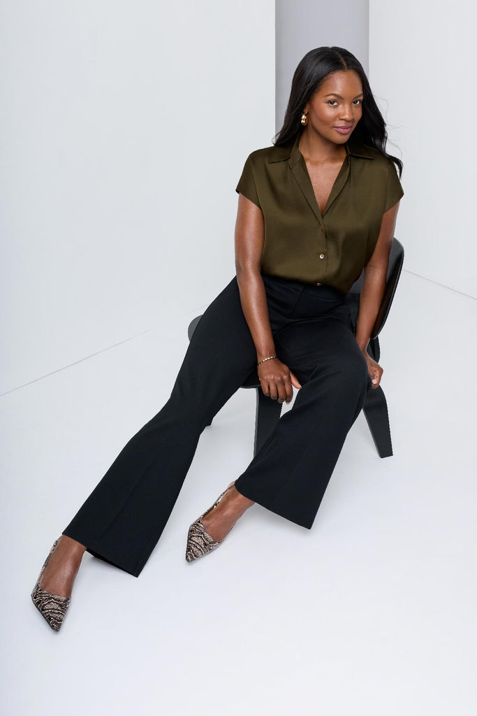 Woman on chair wearing a green button-down blouse with short sleeves and black dress pants