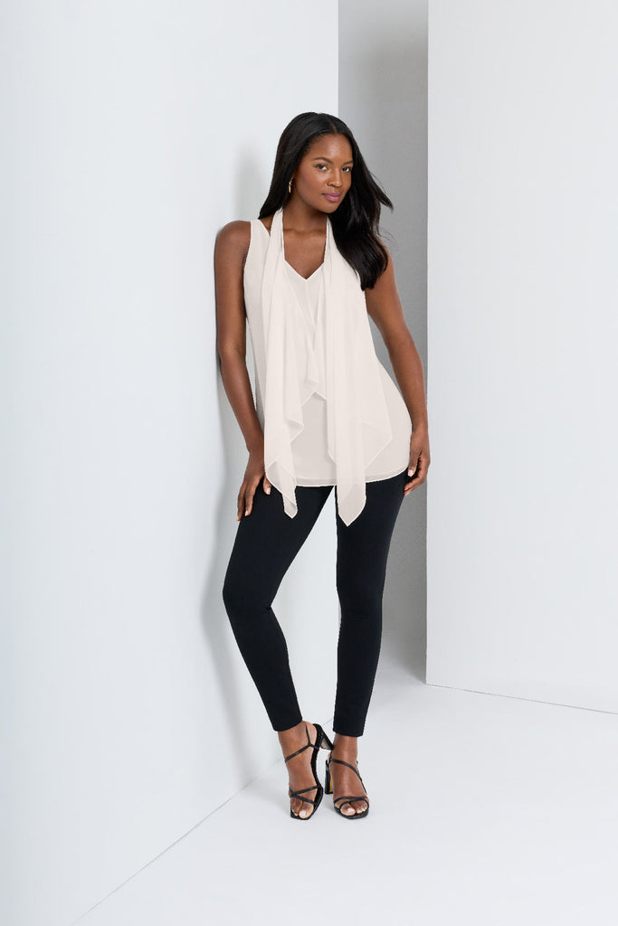 Woman next to wall wearing a white tunic blouse with black leggings