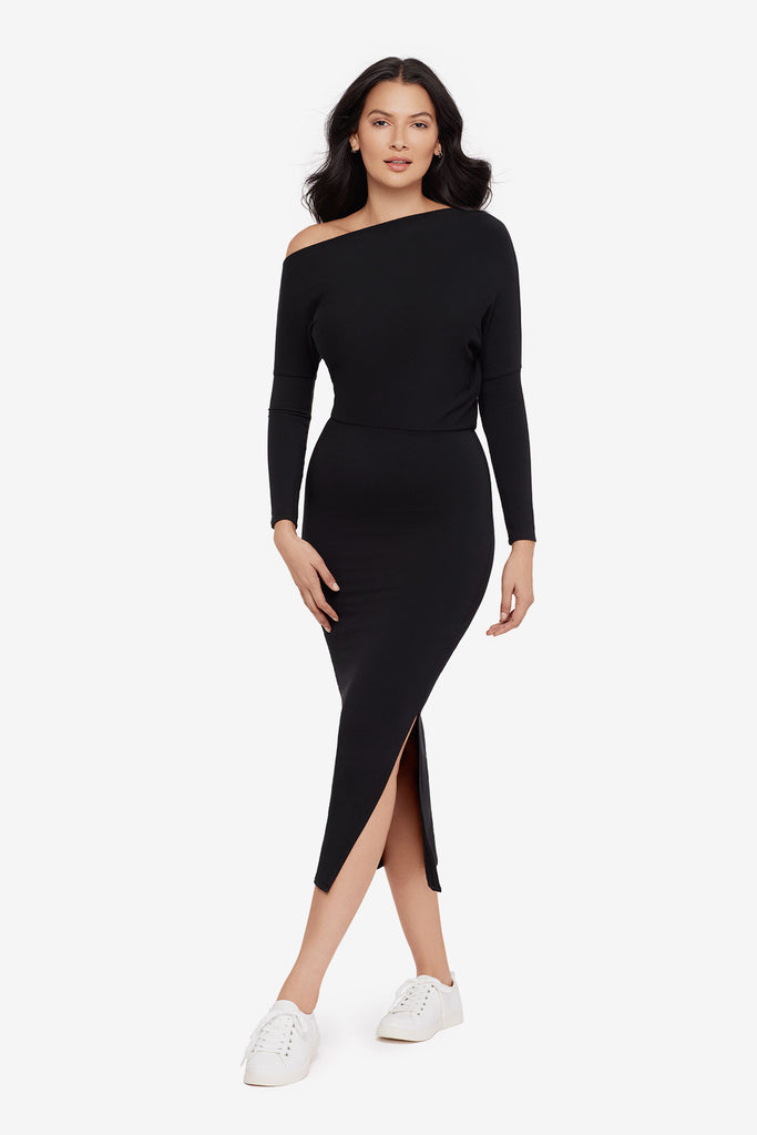 Woman wearing a black asymmetrical off the shoulder long sleeve dress with side slit